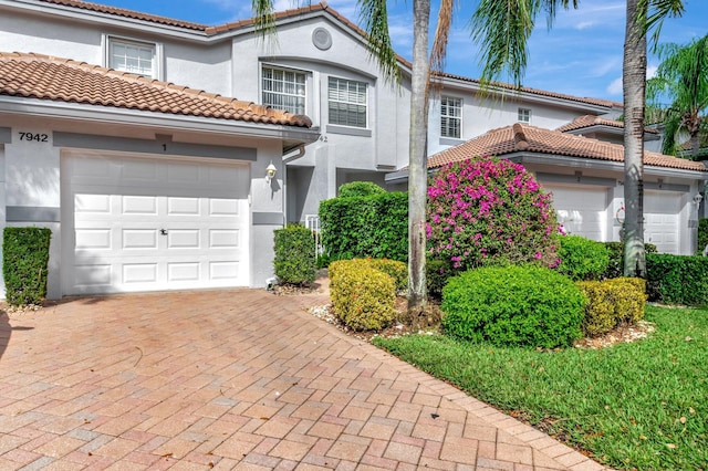 mediterranean / spanish-style house with decorative driveway, a tile roof, an attached garage, and stucco siding