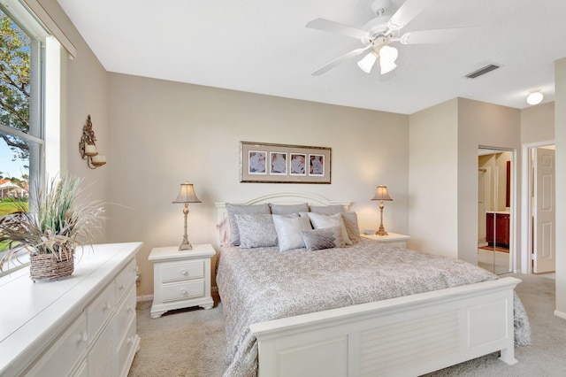 bedroom with light carpet, visible vents, ensuite bath, and ceiling fan