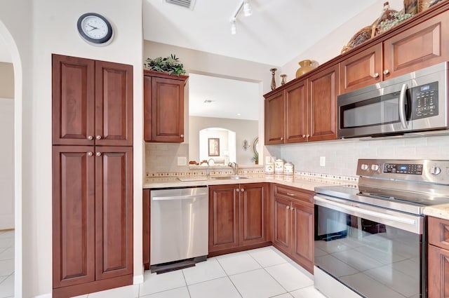 kitchen featuring tasteful backsplash, light tile patterned floors, appliances with stainless steel finishes, arched walkways, and a sink