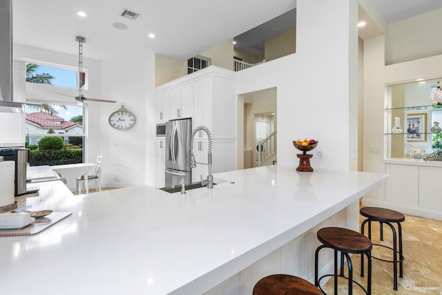 kitchen featuring stainless steel fridge, visible vents, white cabinets, a kitchen breakfast bar, and a sink