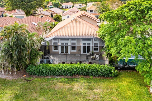 rear view of property featuring a tile roof, a patio, a lawn, glass enclosure, and fence