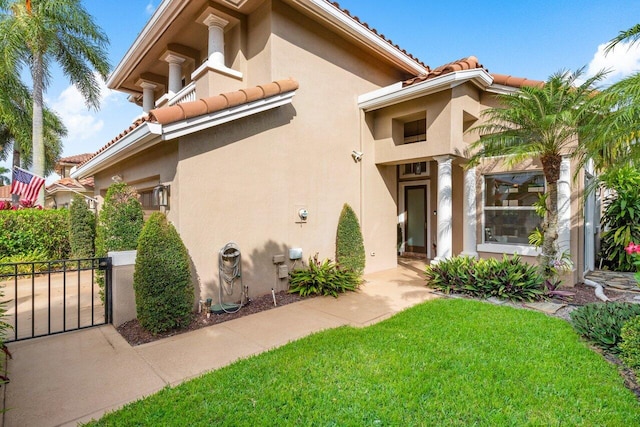 doorway to property featuring a tile roof, a lawn, and stucco siding