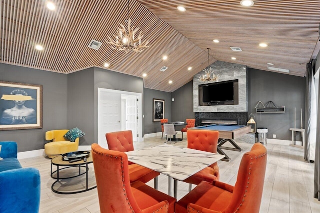 dining space with light wood-style flooring, a large fireplace, visible vents, baseboards, and vaulted ceiling