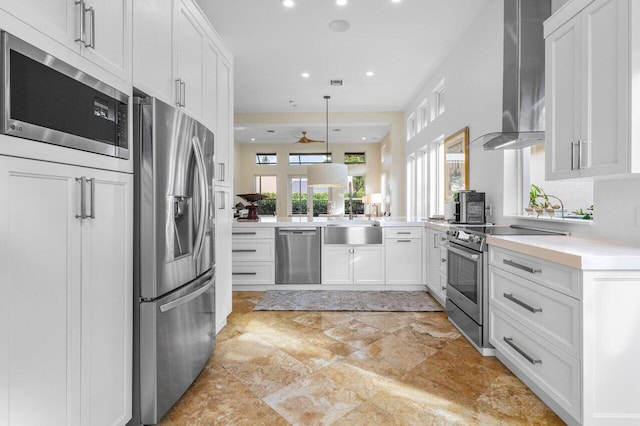 kitchen featuring wall chimney range hood, appliances with stainless steel finishes, a wealth of natural light, and a sink