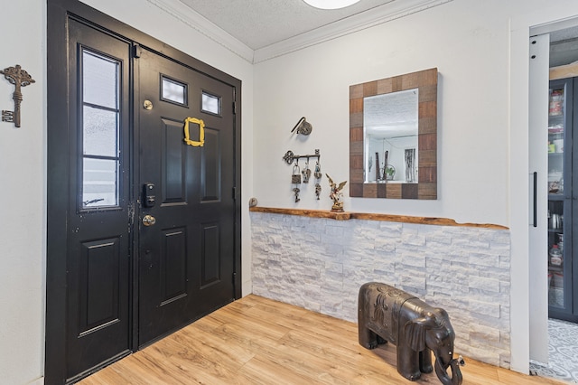 foyer entrance with a textured ceiling, ornamental molding, and wood finished floors