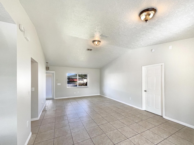 unfurnished room with vaulted ceiling, a textured ceiling, light tile patterned flooring, and baseboards