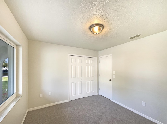 unfurnished bedroom featuring a textured ceiling, carpet floors, visible vents, baseboards, and a closet