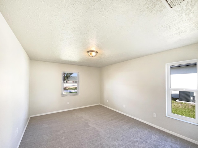 empty room featuring carpet, visible vents, a textured ceiling, and baseboards