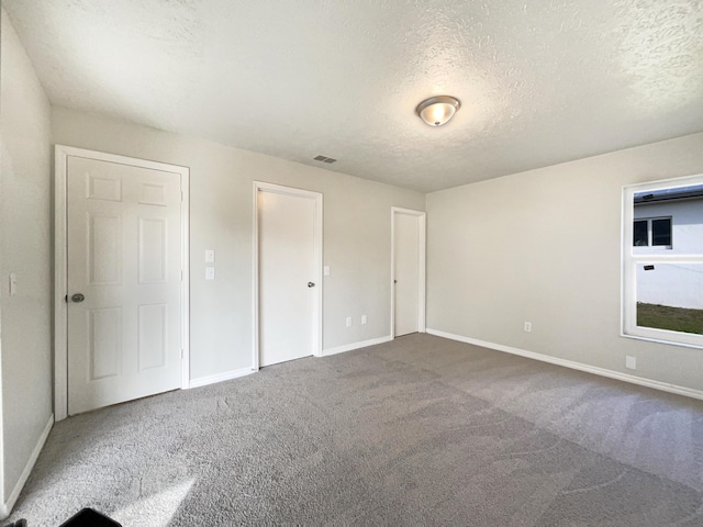 unfurnished bedroom featuring carpet floors, visible vents, a textured ceiling, and baseboards