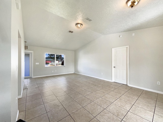 spare room featuring lofted ceiling, visible vents, light tile patterned flooring, a textured ceiling, and baseboards