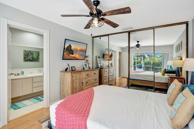 bedroom featuring light wood finished floors, ensuite bath, visible vents, and a ceiling fan