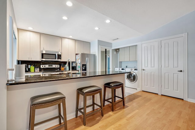 kitchen with light wood-style flooring, washer / clothes dryer, a breakfast bar, stainless steel appliances, and a sink