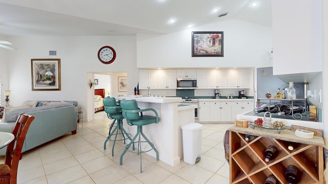 kitchen with appliances with stainless steel finishes, open floor plan, a kitchen breakfast bar, light countertops, and high vaulted ceiling