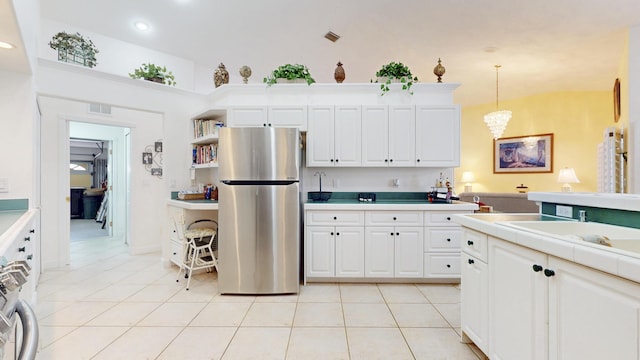 kitchen with light tile patterned flooring, a sink, white cabinets, hanging light fixtures, and freestanding refrigerator