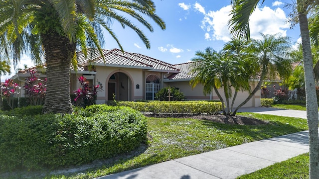 mediterranean / spanish house with a garage, a tile roof, concrete driveway, stucco siding, and a front lawn