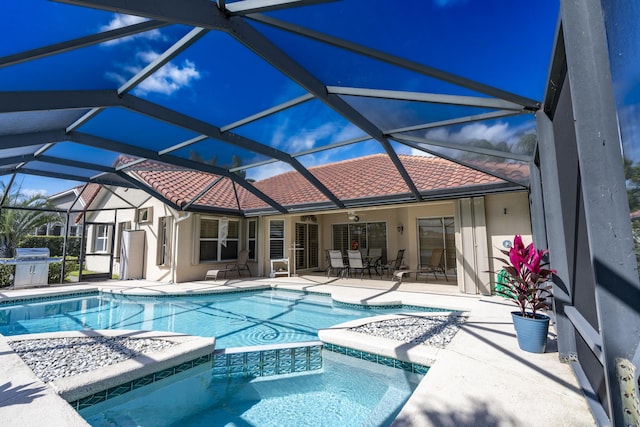 view of swimming pool with glass enclosure, ceiling fan, a pool with connected hot tub, and a patio