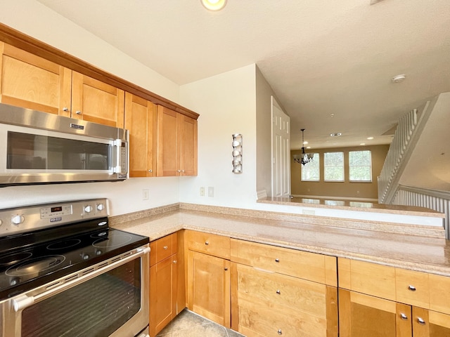 kitchen with brown cabinetry, a peninsula, an inviting chandelier, stainless steel appliances, and light countertops