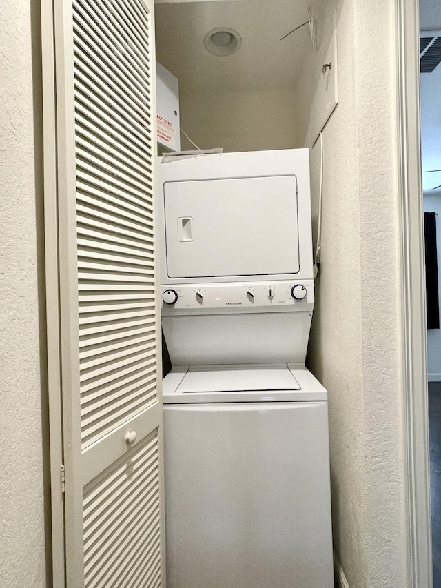 laundry room featuring stacked washer / dryer, laundry area, and a textured wall