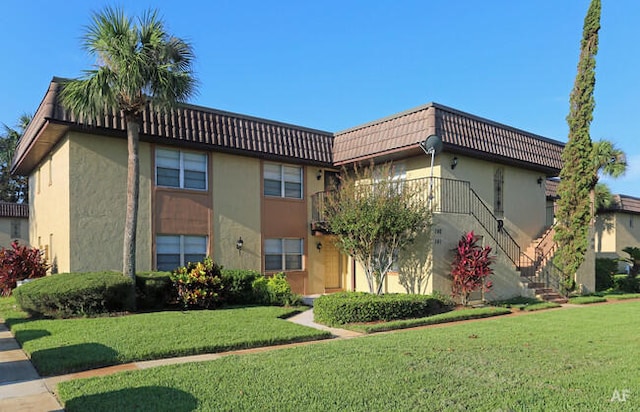 exterior space featuring a tile roof, stairway, a front lawn, and stucco siding