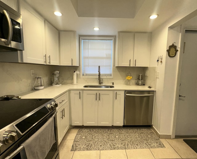 kitchen featuring light tile patterned floors, stainless steel appliances, light countertops, white cabinetry, and a sink