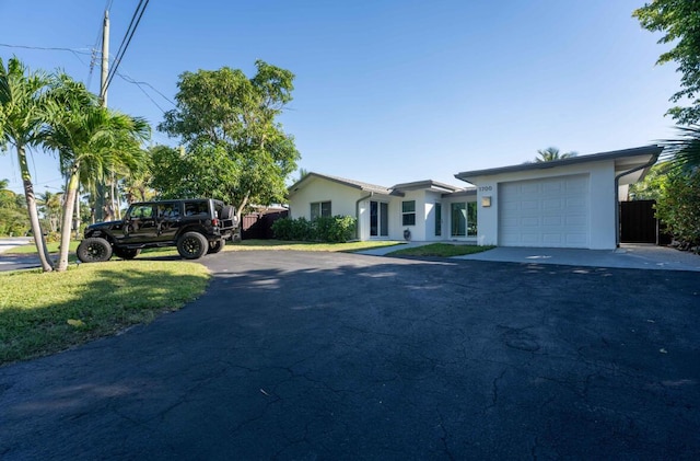 view of front of house with stucco siding, a front lawn, aphalt driveway, fence, and an attached garage