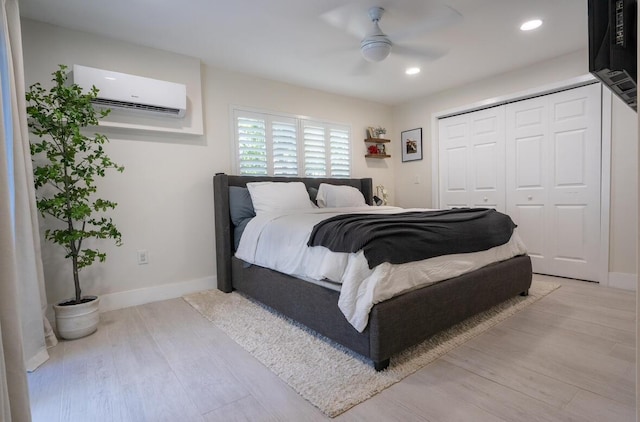 bedroom featuring a closet, wood finished floors, baseboards, and a wall mounted air conditioner