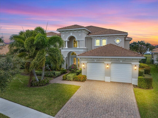 mediterranean / spanish home featuring a yard, decorative driveway, an attached garage, and stucco siding