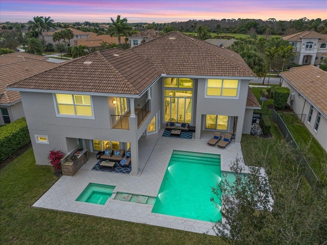 back of house at dusk with a patio, a balcony, a fenced backyard, an outdoor hangout area, and a pool with connected hot tub