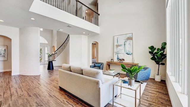 living room featuring arched walkways, a towering ceiling, baseboards, and wood finished floors