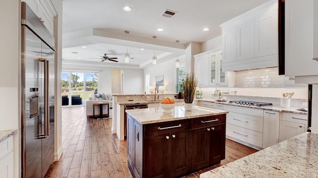 kitchen featuring dark brown cabinetry, glass insert cabinets, open floor plan, hanging light fixtures, and stainless steel appliances