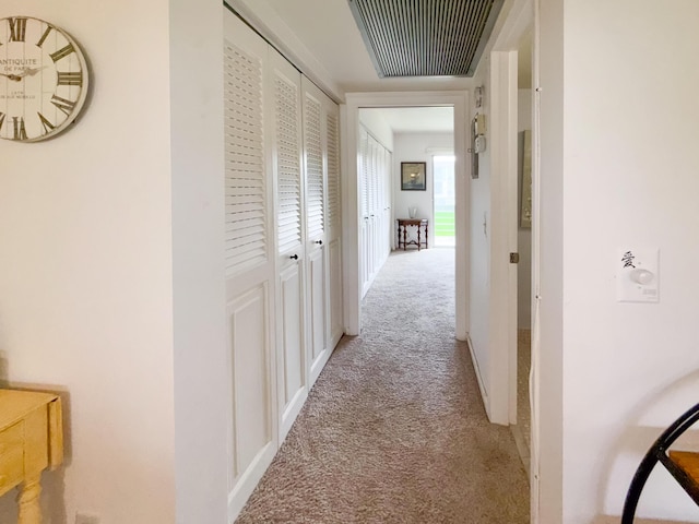 hall featuring baseboards, visible vents, and light colored carpet