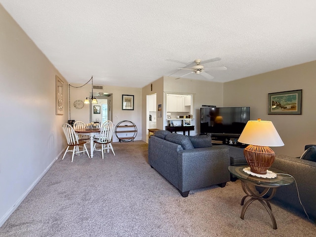 carpeted living area featuring a textured ceiling, ceiling fan, and baseboards