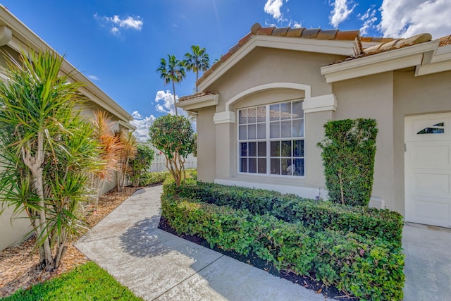 doorway to property featuring a tiled roof, an attached garage, and stucco siding