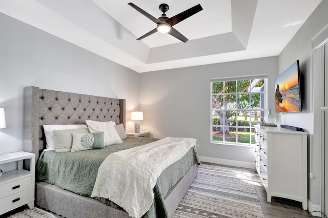 bedroom featuring light wood-style floors, a tray ceiling, baseboards, and a ceiling fan