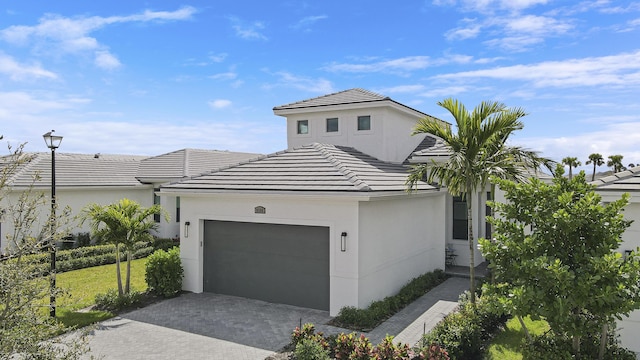 view of front facade featuring a garage, decorative driveway, a tile roof, and stucco siding