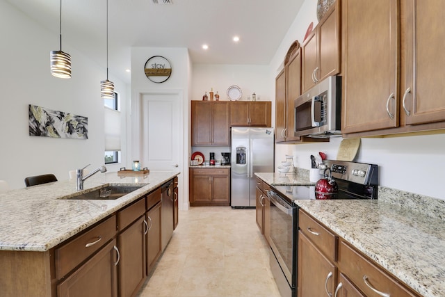 kitchen with appliances with stainless steel finishes, light stone counters, a sink, and decorative light fixtures