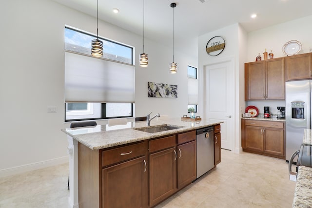 kitchen featuring light stone counters, appliances with stainless steel finishes, a kitchen island with sink, pendant lighting, and a sink