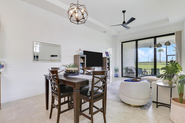 dining space with ceiling fan with notable chandelier, light tile patterned floors, a raised ceiling, and baseboards