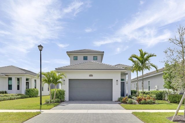 view of front of house with an attached garage, stucco siding, decorative driveway, and a front yard