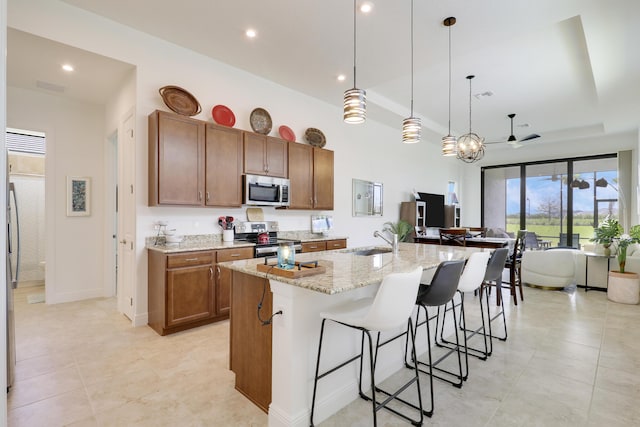 kitchen featuring a breakfast bar area, appliances with stainless steel finishes, brown cabinets, light stone countertops, and a tray ceiling