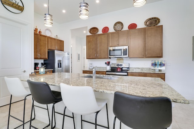 kitchen featuring brown cabinetry, an island with sink, appliances with stainless steel finishes, a breakfast bar, and a sink