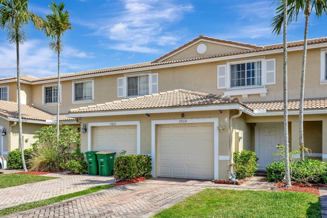 view of property with a garage, decorative driveway, a tile roof, and stucco siding