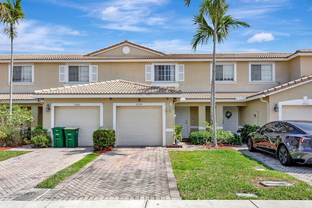 townhome / multi-family property with driveway, a tile roof, and stucco siding