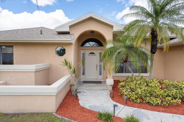 entrance to property featuring roof with shingles and stucco siding