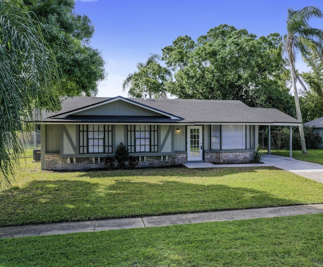 view of front of house with driveway, an attached carport, roof with shingles, a front yard, and brick siding