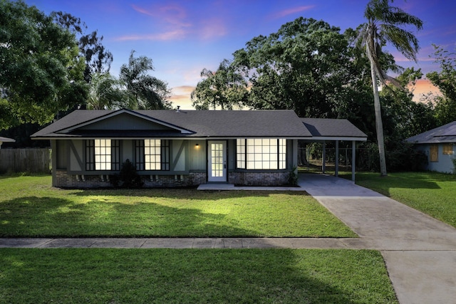 view of front facade featuring concrete driveway, roof with shingles, a carport, and a yard