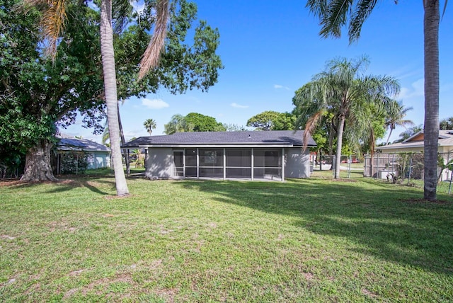 rear view of house featuring a sunroom, a yard, and fence