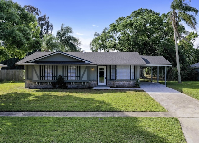 single story home with a shingled roof, concrete driveway, an attached carport, a front yard, and brick siding