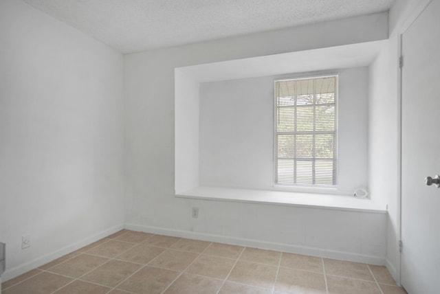 unfurnished room with a textured ceiling, light tile patterned flooring, and baseboards