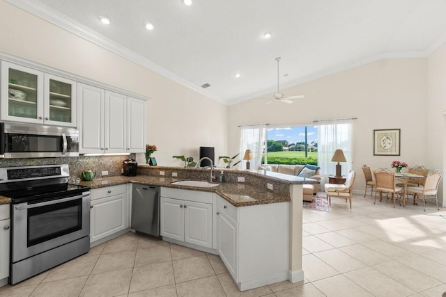 kitchen with stainless steel appliances, a peninsula, a sink, white cabinetry, and dark stone countertops